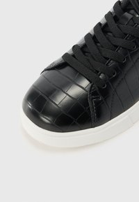 Black sneaker made of textured, croc-embossed material with black laces, rounded toe, and white rubber sole.