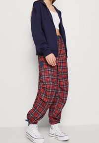 Sudadera con cremallera en color navy combinada con pantalones baggy de cuadros rojos que cuentan con bolsillos, puños elásticos y zapatillas altas blancas.