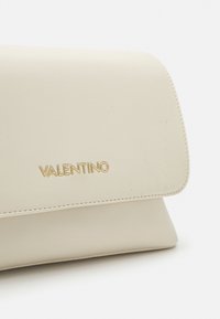 Gräddfärgad läderkuvertväska med en vikbar design, som har en gyllene "Valentino"-logotyp och subtila sömnadsdetaljer.