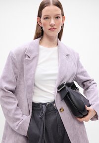 Fialový kordurový blazer s klopovými límci, zapínanie na gombík; biele tričko pod ním, skombinované so šedými nohavicami s vysokým pásom a čiernou kabelkou.