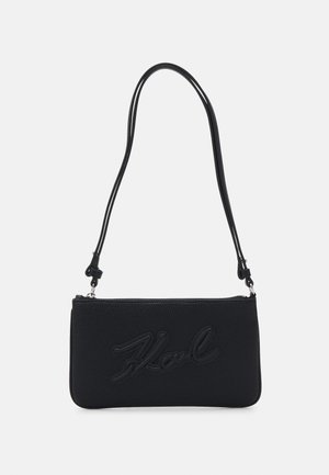 Sac à bandoulière en cuir noir rectangulaire avec une longue bandoulière réglable et la signature "Karl" embossée sur le devant.