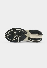 Σόλα New Balance sneaker που δείχνει μαύρο και μπεζ πέλμα με υφή και όνομα της μάρκας στην περιοχή της φτέρνας.