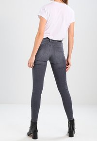 Höga grå skinny jeans med en slät textur, som har en bakre yoke och två fickor. Kombineras med en vit t-shirt och svarta ankelstövlar.