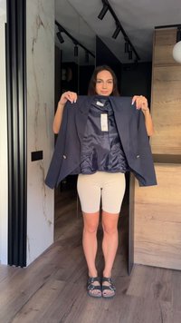 Femme debout à l'intérieur tenant un blazer bleu marine ouvert montrant sa doublure intérieure et l'étiquette de prix.