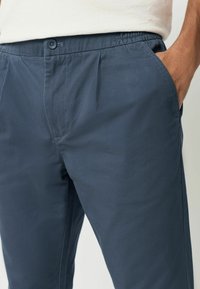 Navyblaue Hosen aus leichtem Stoff, mit elastischem Bund, Knopfverschluss und Seitentaschen. Strukturiertes Oberflächendetail.