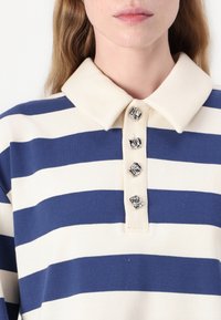 Navy and cream striped polo shirt with a classic collar and four decorative silver buttons at the placket. Soft cotton material.