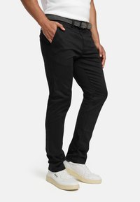Pantaloni neri aderenti in misto cotone, con cintura intrecciata strutturata e tasche laterali. Abbinati a sneakers bianche per creare contrasto.