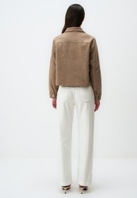 Veste courte marron en tissu doux avec un col, un empiècement au dos et des poignets boutonnés, associée à un pantalon blanc taille haute.