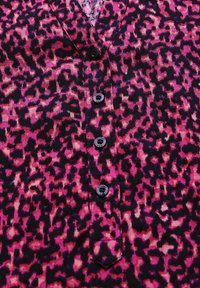 Rosa och svart leopardskinnstyg med en subtil textur, med en v-ringning och fem svarta knappar fram.