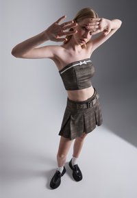 Brown plaid cropped tube top with white accent bow; matching pleated mini skirt with belt; paired with black shoes and white socks.
