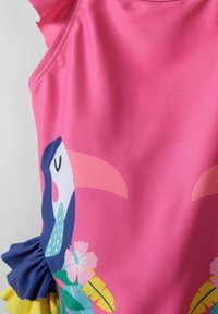 Maillot de bain rose avec un motif de toucan. Accent volants en bleu, avec des motifs floraux et de feuilles dans des couleurs vibrantes. Texture de tissu lisse.
