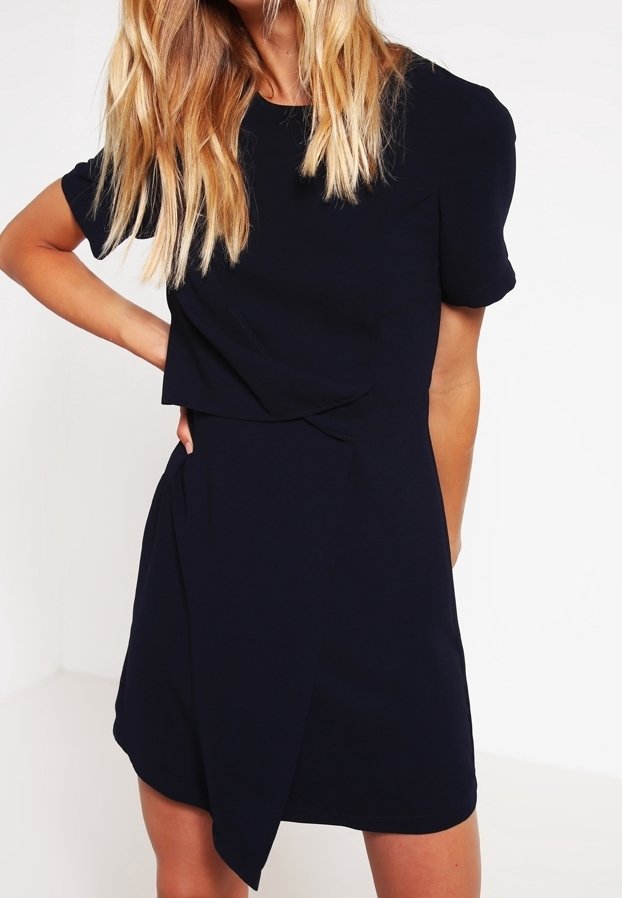 Robe bleu marine à manches courtes avec un design croisé et un ourlet arrondi, fabriquée en tissu léger, avec une texture lisse.