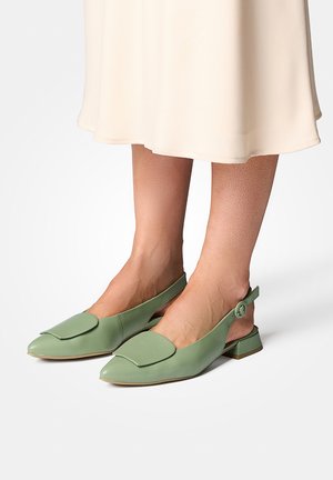 Kvinde iført lysegrønne slingback-sko med lav hæl og spids tå med en klapdetalje, kombineret med en cremefarvet midinederdel.