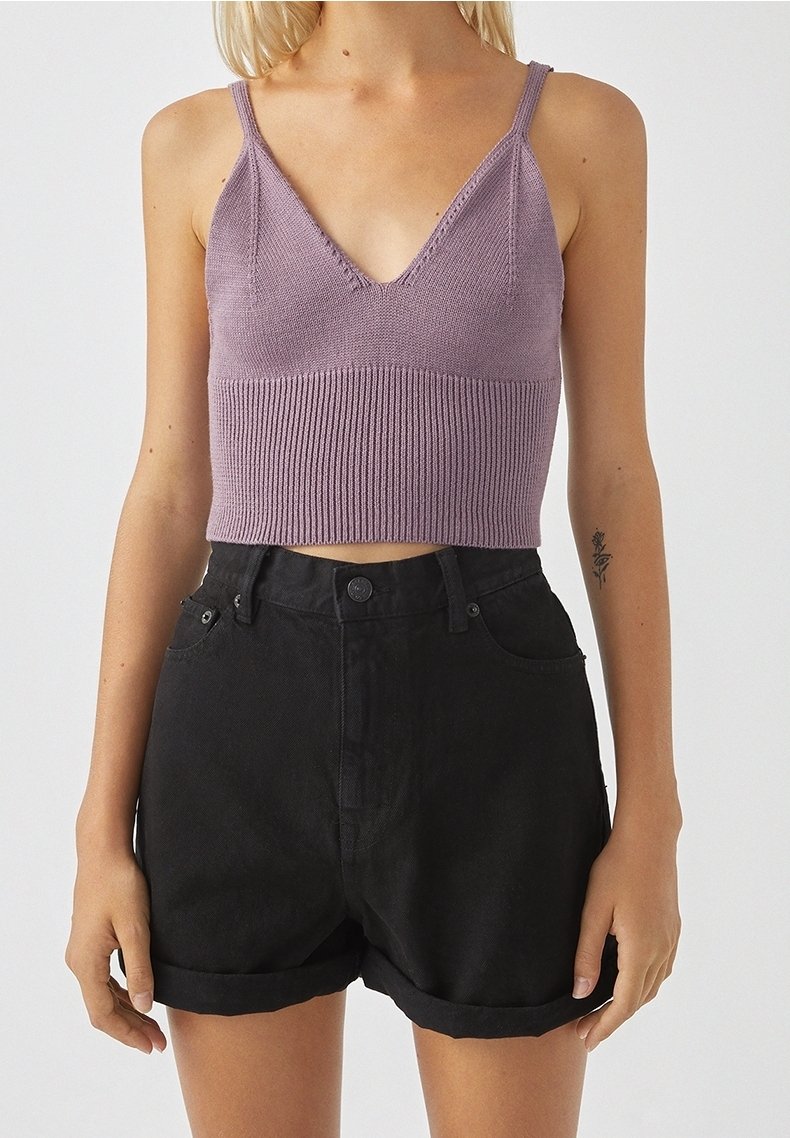 Top sin mangas de punto morado con escote en V y textura acanalada, combinado con pantalones cortos de mezclilla negra de tiro alto y doblados.