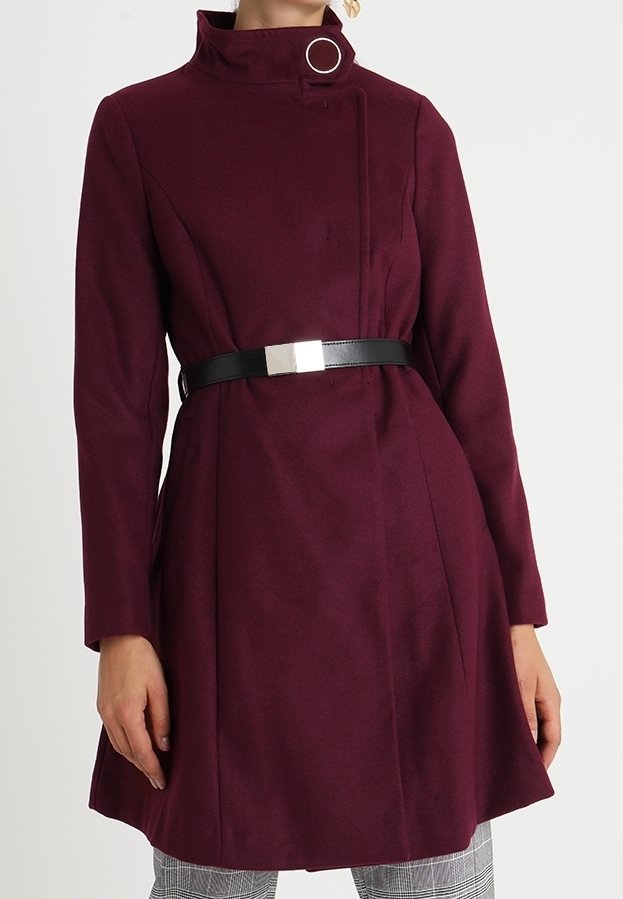 Burgundské vlněné sako s vysokým límcem, dlouhými rukávy a černým páskem se stříbrnou geometrickou sponou; hladká textura s čistými liniemi.
