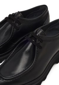 Zwarte leren schoenen met een gladde afwerking, ronde vorm, zwarte veters en een robuuste zool. Heeft gestikte accenten op de bovenkant.