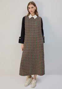 Juoda be rankovių su raštais su balta apykakle, puošta daugiaspalviu geometriniu raštu. Turi kišenes ir laisvą siluetą.