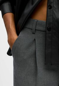 Grijze op maat gemaakte broek in een zachte textuur, met een vlakke voorkant, zijzakken en een gedeeltelijk zichtbare zwarte leren blouse.