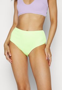 Parte de baixo de biquíni de cintura alta em tecido canelado neon verde. Apresenta uma textura suave e uma cor sólida com um acabamento contrastante em roxo na parte superior.