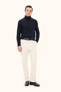 Marineblauer Rollkragenpullover, cremefarbene Hose und schwarze Lederschuhe. Das Outfit zeichnet sich durch ein figurbetontes Design und minimale Akzente aus.