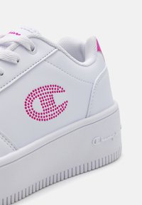 Sneakers platform bianchi con una tomaia sintetica liscia, dotate di un logo a pois rosa e un accento rosa sul tallone. Suola in gomma texturizzata.