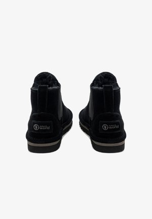 Schwarze Wildleder-Stiefeletten mit einem weichen Innenfutter, elastischen Seiteneinsätzen und einer Gummisohle, die über eine kontrastierende beigefarbene Kante und Beschriftung verfügt.