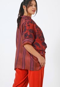 Chemise surdimensionnée rouge et violette avec un motif floral, manches courtes et accents rayés. Assortie à un pantalon rouge uni, avec une texture lisse.