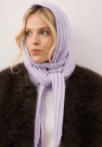 Lila gebreide sjaal met een geribbelde textuur, om de hals gebonden, met een zachte uitstraling en een subtiele glans, gedragen over een donker bontjas.