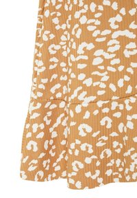 Tissu brun clair avec un motif léopard blanc irrégulier et une couture visible près du bord inférieur d'un vêtement.