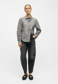 Stribet skjorte i grå og hvid, parret med h�øjtaljede mørkegrå jeans. Fodtøj med sorte flade sko med sløjfer.