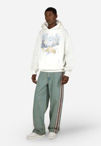 Der weiße Hoodie hat einen grafischen Druck mit Tieren und Bäumen. Die weit geschnittenen blauen Jeans verfügen über eine seitliche Streifendetail. Weiße Sneakers runden den Look ab.