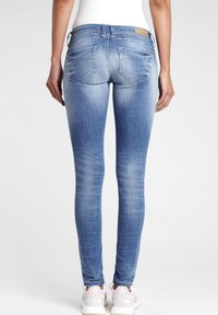 Osoba v světle modrých zesvětlených skinny jeans a bílých a růžových teniskách, stojící s uvolněnýma rukama podél těla, čelí dozadu.