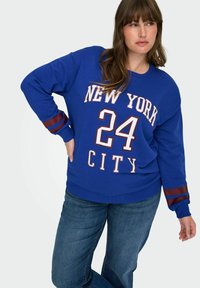 Kraljevsko plava dukserica sa natpisom "NEW YORK 24 CITY" ispisanom u bijeloj i bordo boji. Sadrži bordo pruge na rukavima. Mekani pamučni miks.