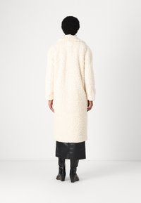 Crème-kleurige shaggy jas met een gestructureerde afwerking, lange mouwen en een kraag. Draag hem over een zwarte leren rok en combineer met zwarte hoge laarzen.