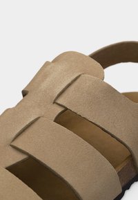 Μπεζ δερμάτινο σανδάλι με φαρδιές αλληλοκαλυπτόμενες λουρίδες και πάτο από φελλό, σχεδιασμένο για καθημερινή χρήση και άνεση.