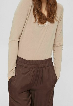 Top beige a maniche lunghe con scollatura a barca e dettagli sottili, abbinato a pantaloni marroni a vestibilità rilassata con vita elasticizzata.
