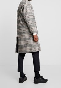 Plaid long coat in gray, black, and white, with slight side slits and ribbed cuffs. Paired with dark trousers and black sneakers.