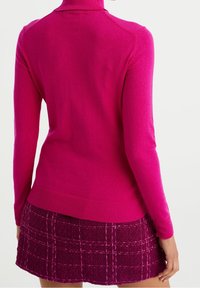 Maglione a collo alto fucsia realizzato in tessuto morbido, con maniche lunghe e polsini a coste, abbinato a una mini gonna a quadri testurizzata in rosa scuro.