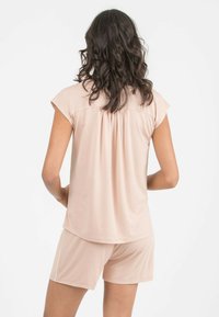 Světlý růžový loungewear set s krátkým rukávem, který má sklady, a odpovídajícími šortkami, vyrobený z měkké a hladké tkaniny.