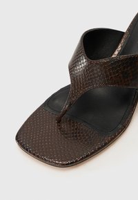 Hnědé sandály typu flip-flop z umělé hadí kůže se čtveratou špičkou a designem s překříženými pásky. Mají hladkou černou stélku a jemný lesk.