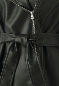 Chaqueta de cuero sintético negro con un frente con cremallera, cintura con cinturón y una textura suave con un patrón de grano visible.