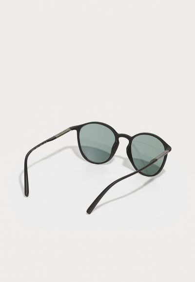 Round black sunglasses with green lenses, slim black arms, and metallic accents on the hinges. Lightweight design, minimalistic style.