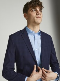 Navy blue, check-patterned suit jacket with a notched lapel, paired with a light blue shirt. Features a single chest pocket and button closure.