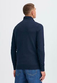 Dunkelblauer Pullover mit langen Ärmeln und hohem Kragen, mit gerippten Bündchen und Saum, aus einem glatten, strukturierten Strickstoff. Ansicht von hinten.