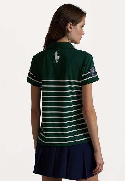 Grønn polo skjorte med hvite horisontale striper, korte ermer, og en liten brodert logo på baksiden. Kombinert med et marineblått plisserte skjørt.