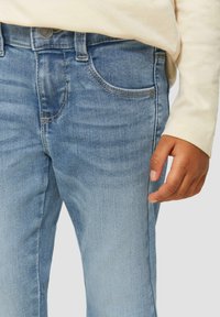 Jeans de denim azul claro con un corte clásico, que cuentan con bolsillos frontales, costuras distintivas y un cierre de botón. Textura suave y lavado medio.