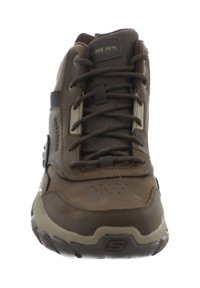 Zapato de senderismo marrón con parte superior de cuero y malla, cordones texturizados y suela de goma. Presenta lados reforzados y agujeros de ventilación en la punta.