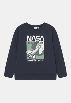 Sweat-shirt bleu marine avec un graphisme NASA représentant une navette spatiale et la Terre. Encolure ronde, manches longues et poignets côtelés. Matière en coton.