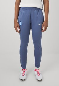 Mannen sportieve blauwe broek van rekbaar materiaal. Bevat een zilveren Nike-logo en een rond blauw teamlogo op het linkerbeen. Fitted design.