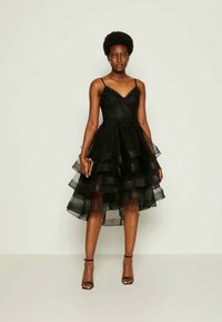 Μαύρο φόρεμα με εφαρμοστή κορυφή και ρυθμιζόμενες τιράντες, με επικαλυμμένες τούλιες στο στρίφωμα και διακοσμητικά στοιχεία από χάντρες στο στήθος.